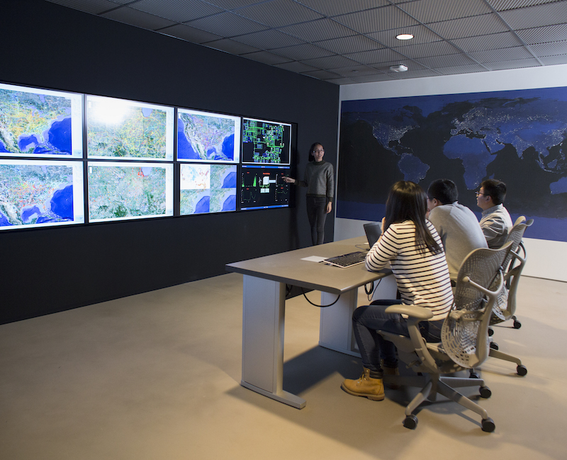 Photo of several people sitting at desk looking at screens with maps