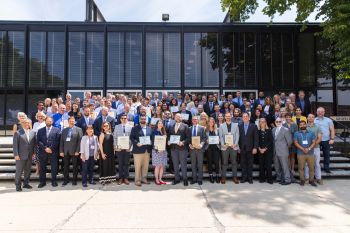 A large group of people pose on steps in front of a glass building.