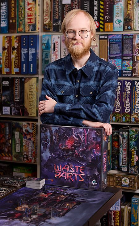 Photo of Evan Duda (Game and Interactive Media Design ’21) posing with his board game, The Waste of Parts.