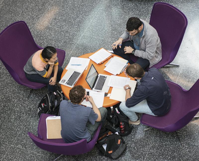 Amour Students gather around a table in the Retaliatta Atrium