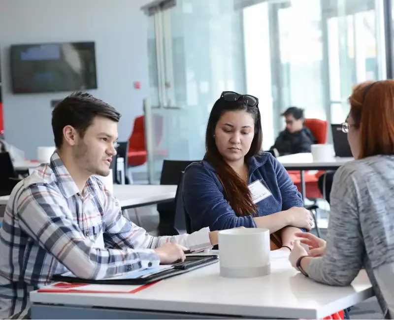 two students sitting around table with advisor across from them